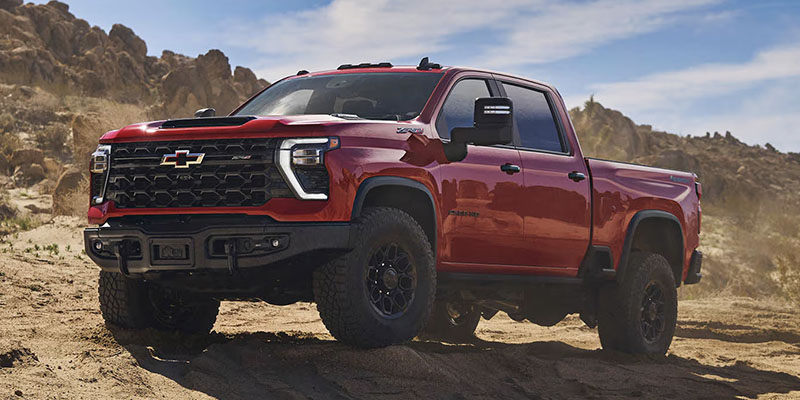 Red Chevrolet Silverado pickup truck on sandy off-road terrain.